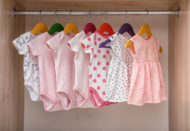 Hangers with baby clothes on rack in wardrobe