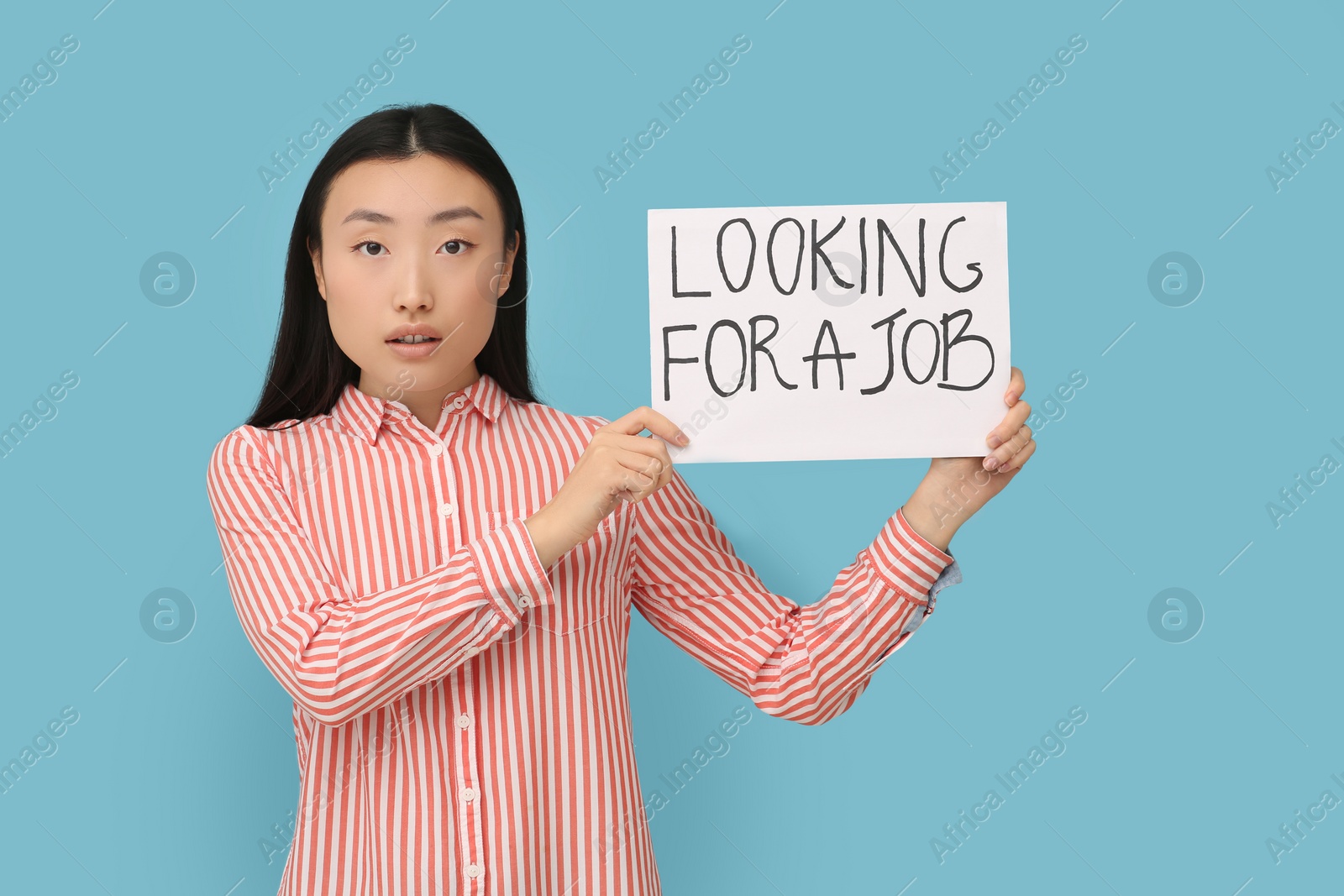 Photo of Unemployed Asian woman holding sign with phrase Looking For A Job on light blue background