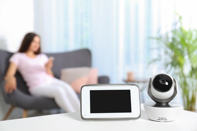 Photo of Baby monitor and camera on table and woman resting in living room. Video nanny