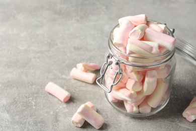 Photo of Glass jar with tasty marshmallows on light grey table, closeup. Space for text