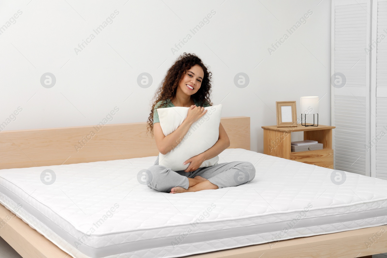 Photo of Happy young African American woman hugging pillow on bed with comfortable mattress at home