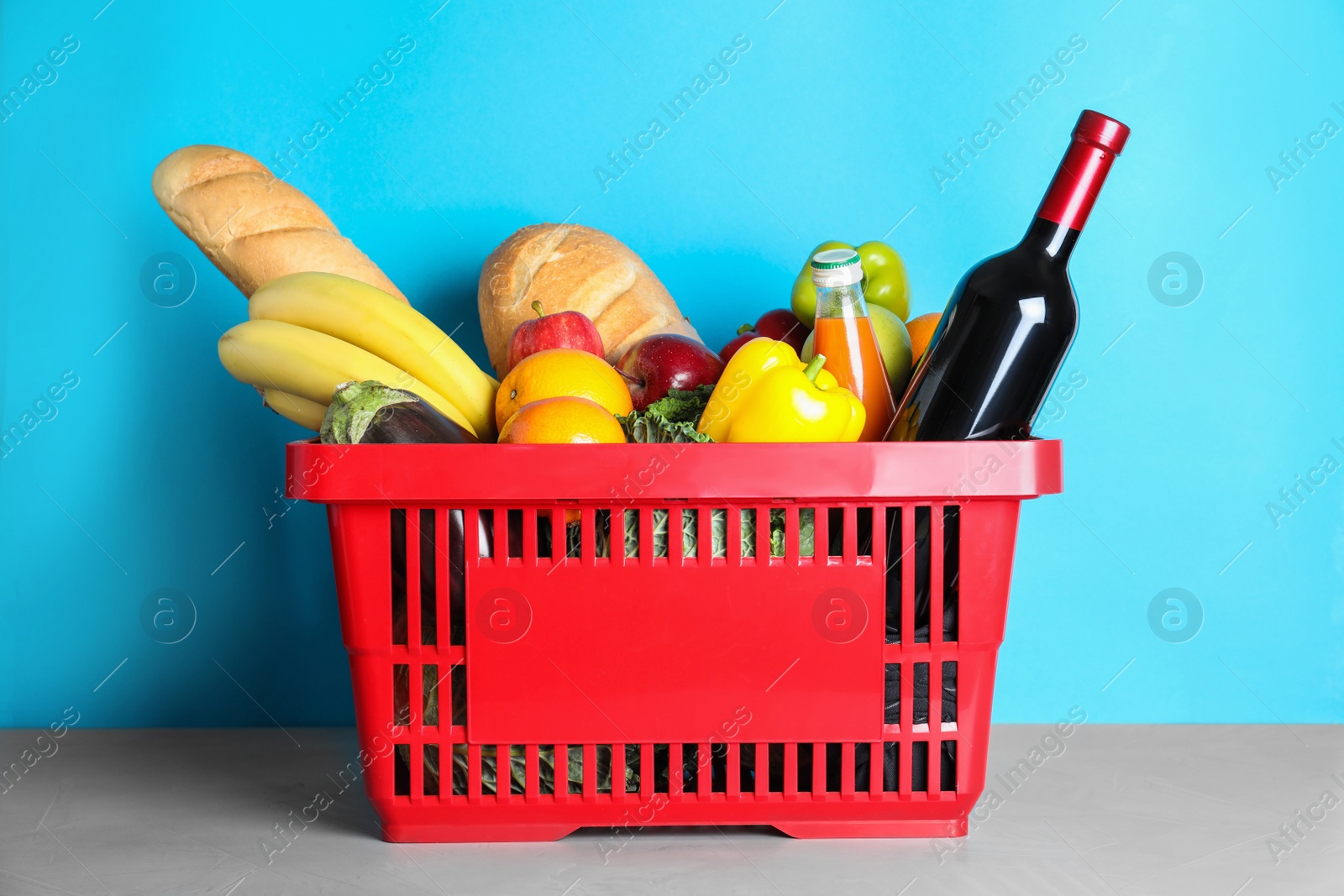 Photo of Shopping basket with grocery products on grey table against light blue background