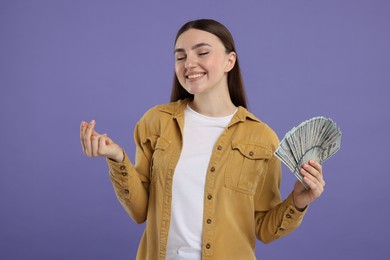 Happy woman with dollar banknotes showing money gesture on purple background