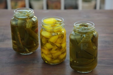 Photo of Glass jars of pickled green and yellow jalapeno peppers on wooden table