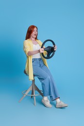 Photo of Emotional young woman on chair with steering wheel against light blue background