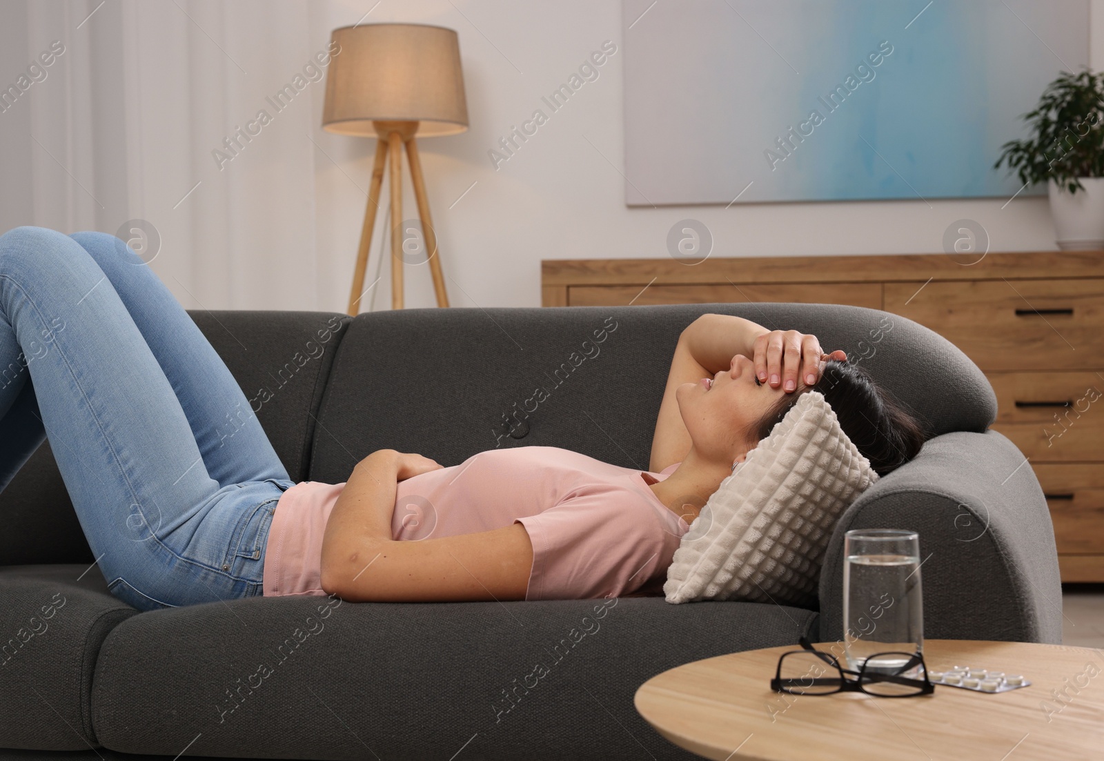 Photo of Sad woman suffering from headache on sofa indoors