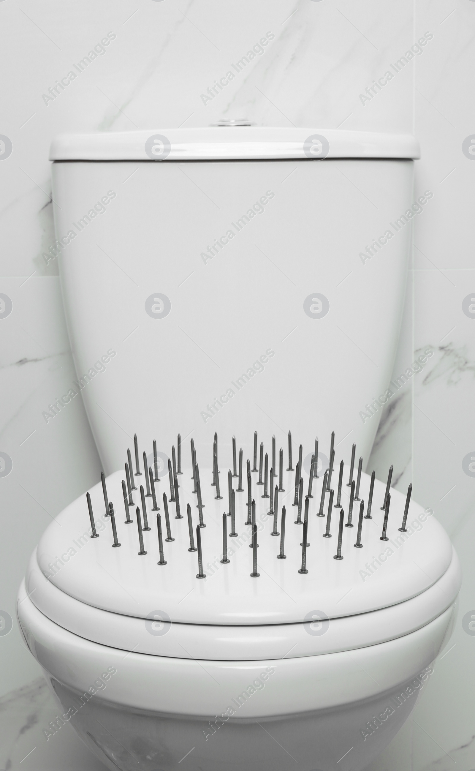 Photo of Toilet bowl with nails near marble wall. Hemorrhoids concept