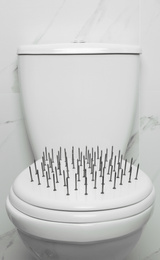 Photo of Toilet bowl with nails near marble wall. Hemorrhoids concept