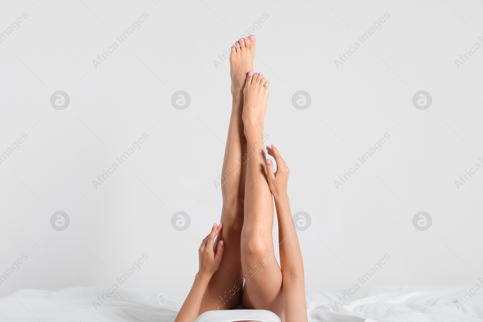 Photo of Woman with beautiful smooth legs on bed against white background, closeup
