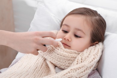 Photo of Mother using nasal spray to treat her little daughter on bed, closeup