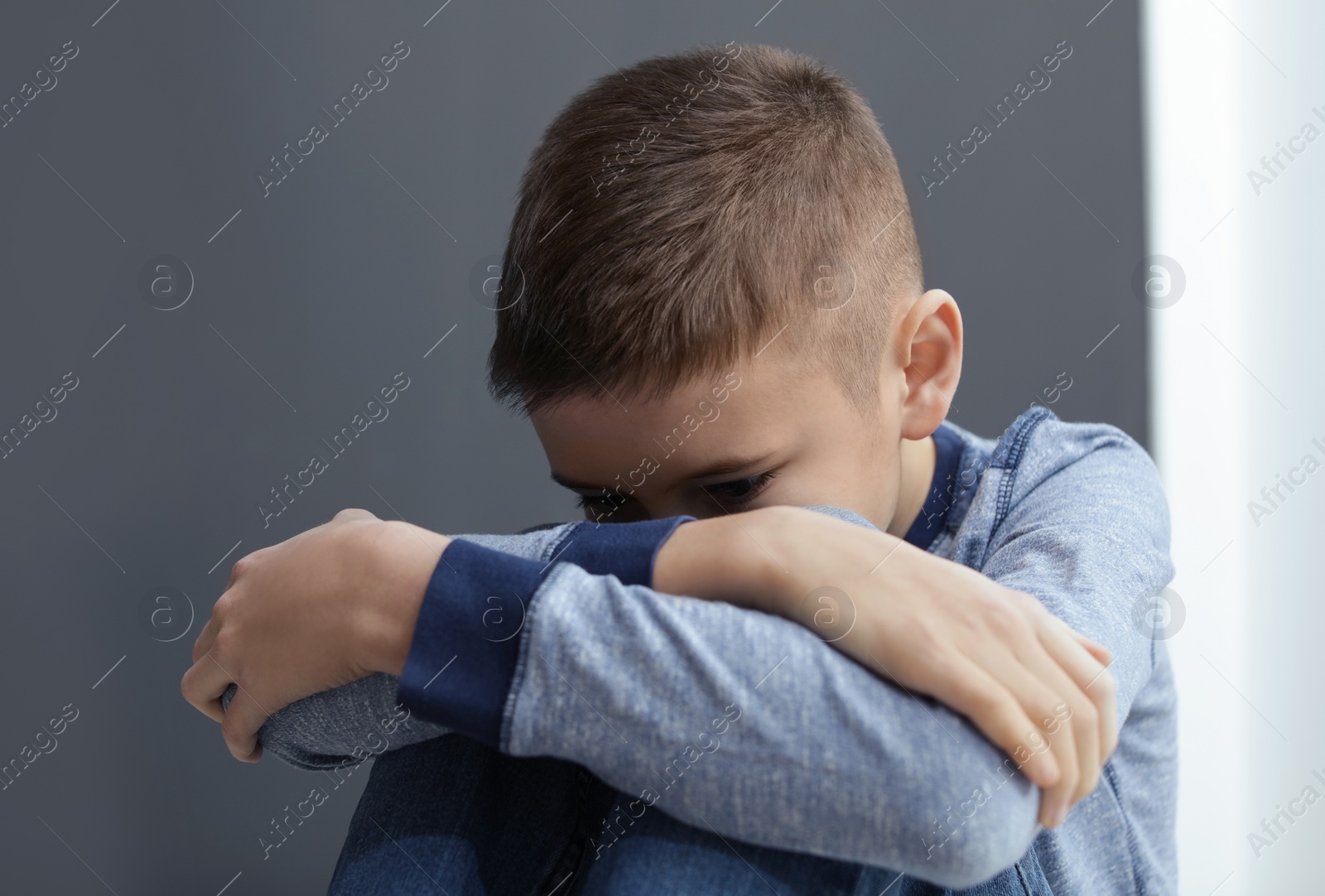 Photo of Upset preteen boy sitting at grey wall indoors