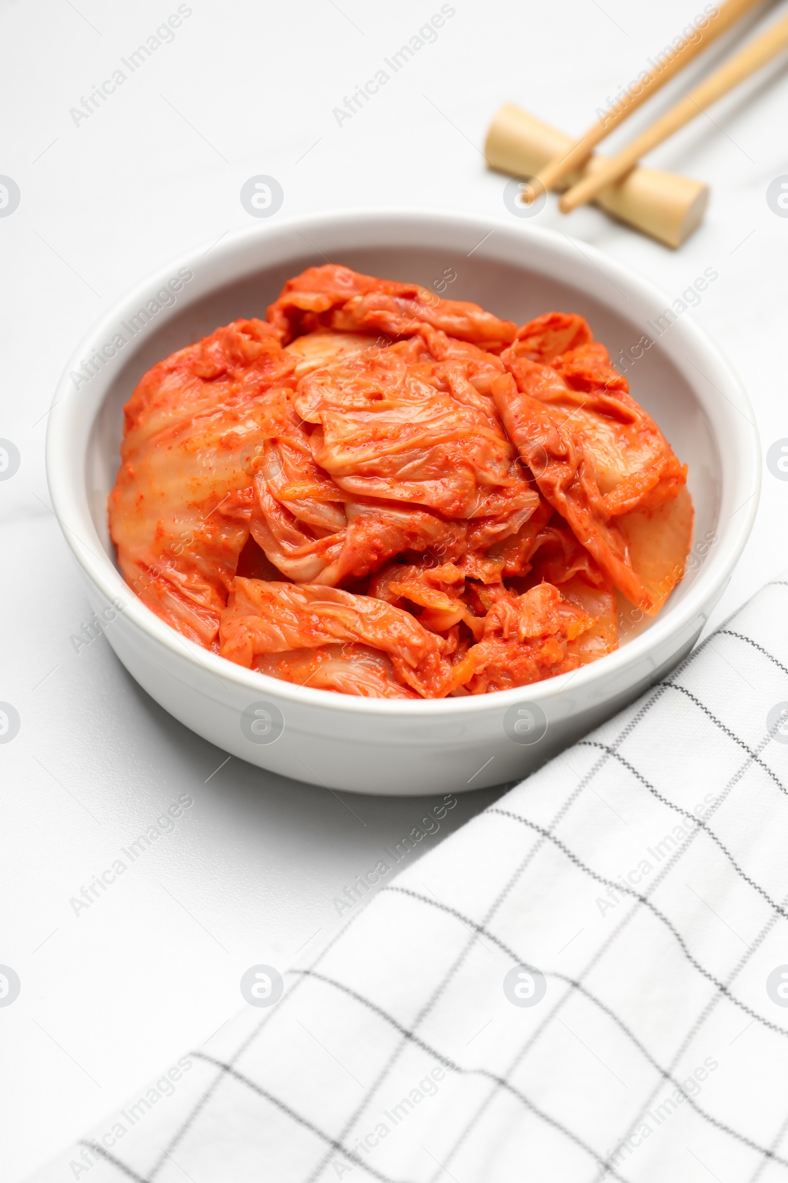 Photo of Bowl of spicy cabbage kimchi and chopsticks on white marble table