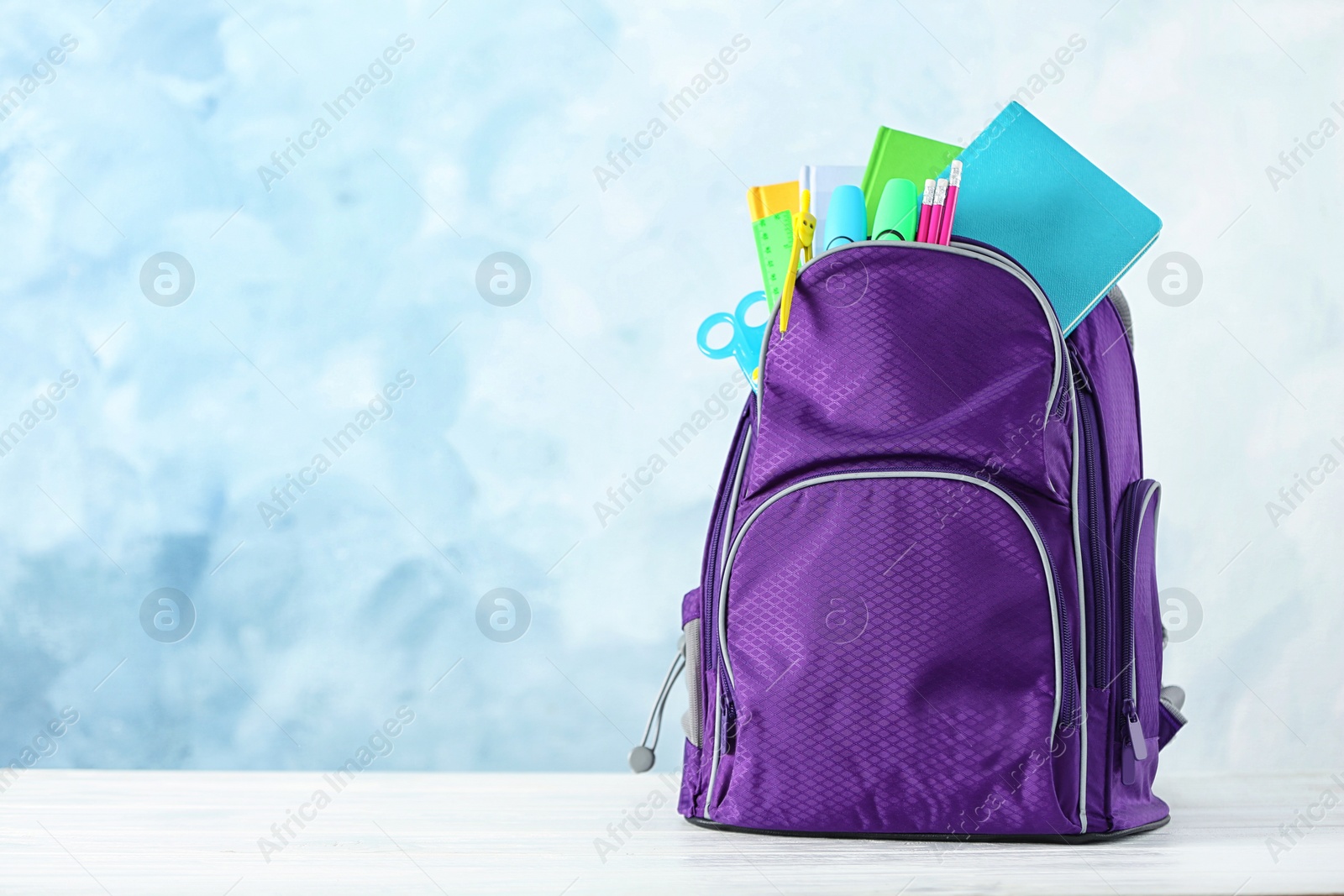 Photo of Backpack with school stationery on table against color background