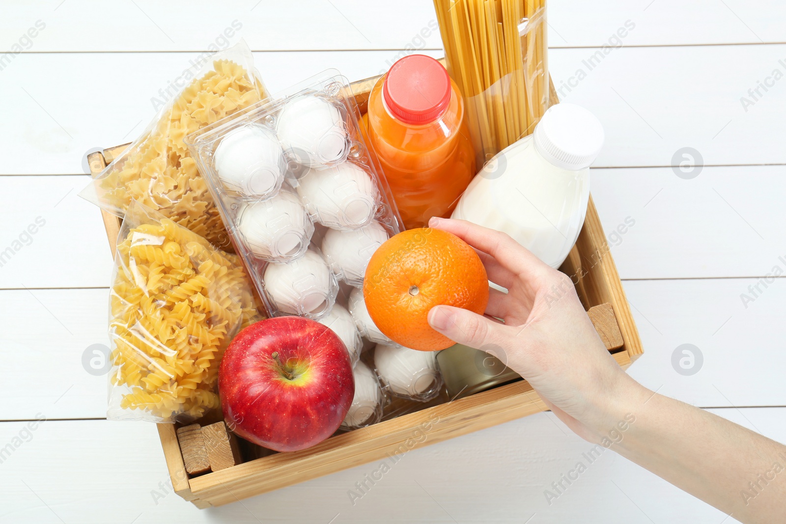 Photo of Humanitarian aid. Woman with food products for donation at white wooden table, top view