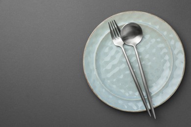 Photo of Clean plate, fork and spoon on grey background, top view. Space for text
