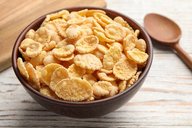 Photo of Bowl of tasty corn flakes and spoon on white wooden table, closeup