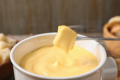 Photo of Dipping bread into pot with cheese fondue on table, closeup