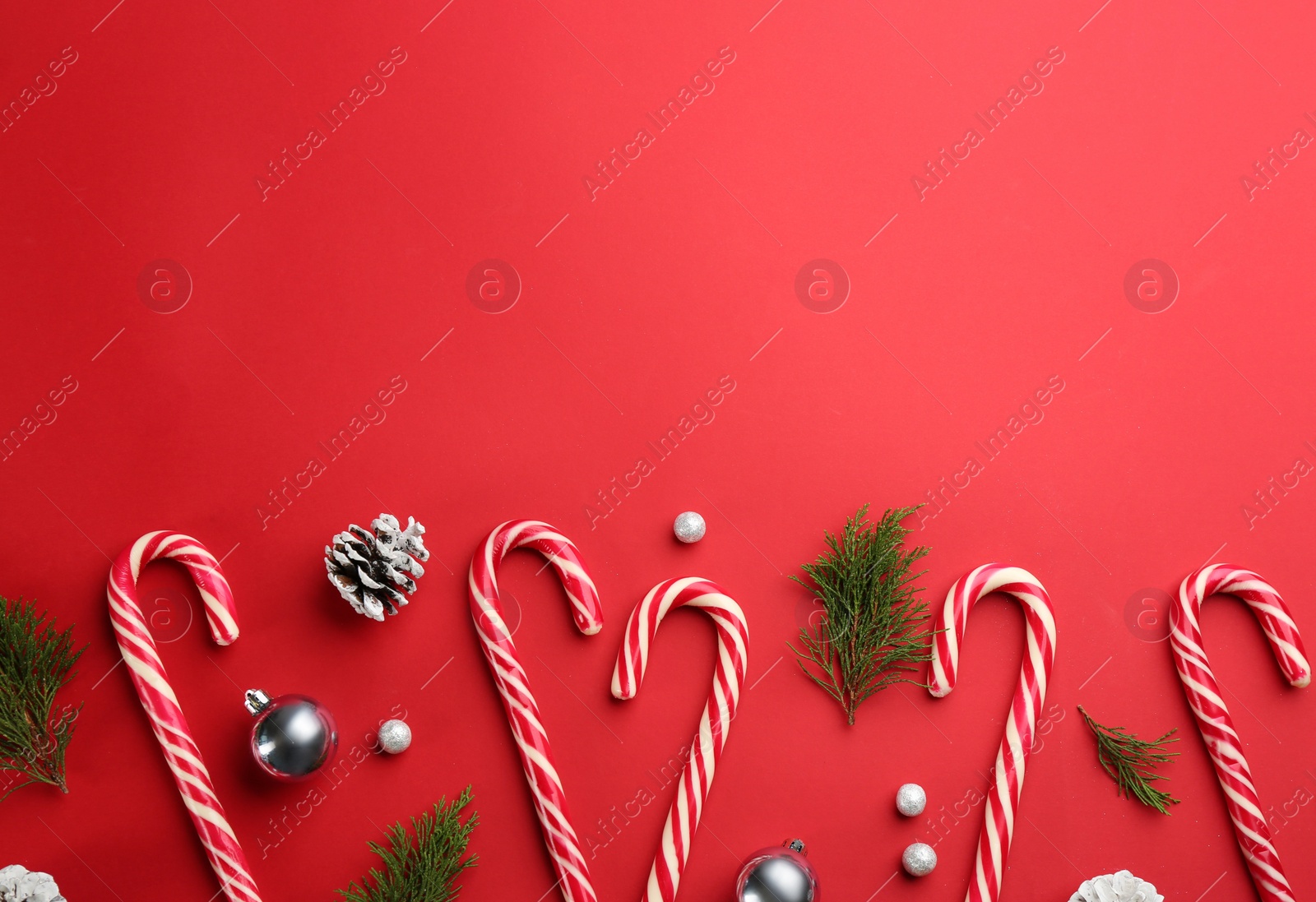 Photo of Flat lay composition with candy canes and Christmas decor on red background. Space for text
