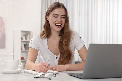 Photo of Happy woman with notebook and laptop at white table in room