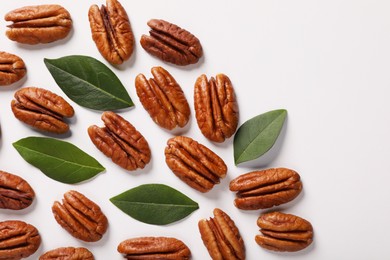 Photo of Delicious pecan nuts and green leaves on white background, flat lay. Space for text