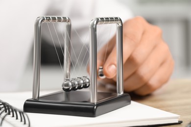 Photo of Man playing with Newton's cradle at table, closeup. Physics law of energy conservation
