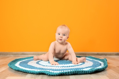 Photo of Cute little baby on soft rug near color wall