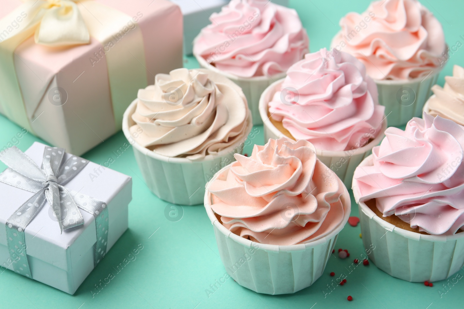 Photo of Delicious birthday cupcakes, gift boxes and sprinkles on turquoise background, closeup