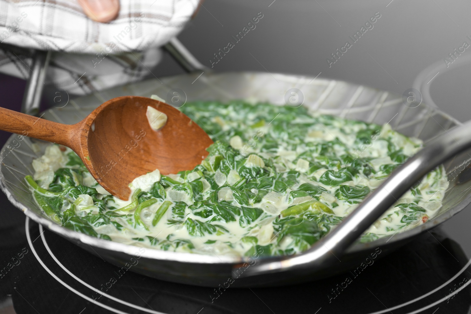 Photo of Woman cooking tasty spinach dip on kitchen stove, closeup view