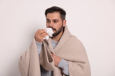 Photo of Sick man wrapped in blanket with tissue on light grey background. Cold symptoms