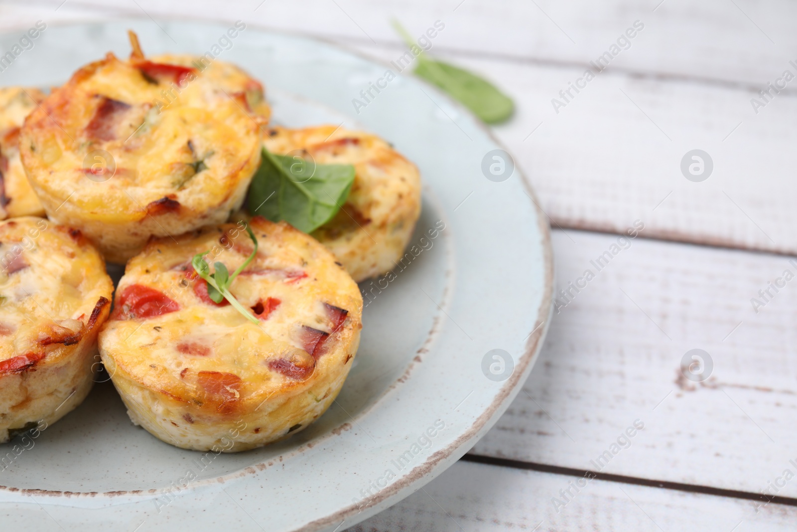 Photo of Delicious egg muffins with cheese and bacon on white wooden table, closeup. Space for text
