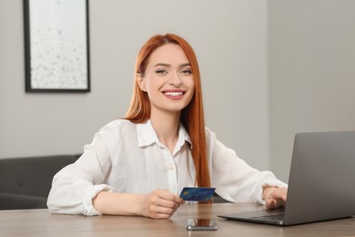 Happy woman with credit card using laptop for online shopping at wooden table in room