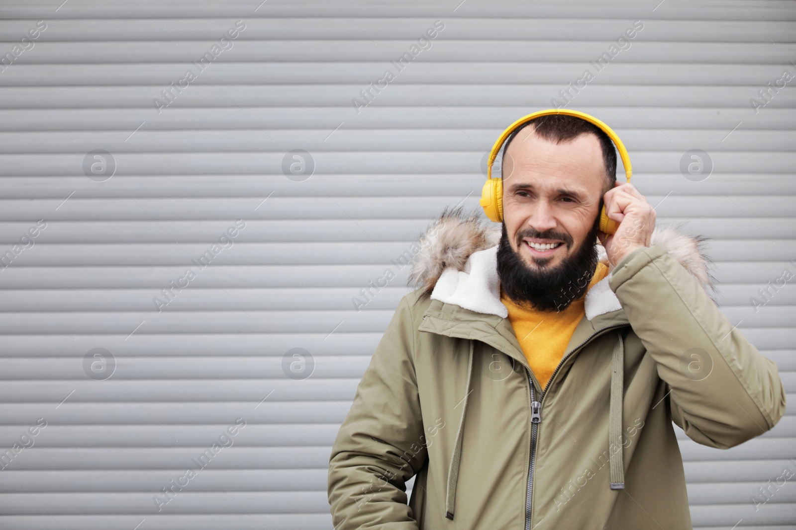 Photo of Mature man with headphones listening to music near light wall. Space for text