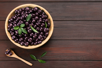 Tasty acai berries in bowl and spoon on wooden table, flat lay. Space for text