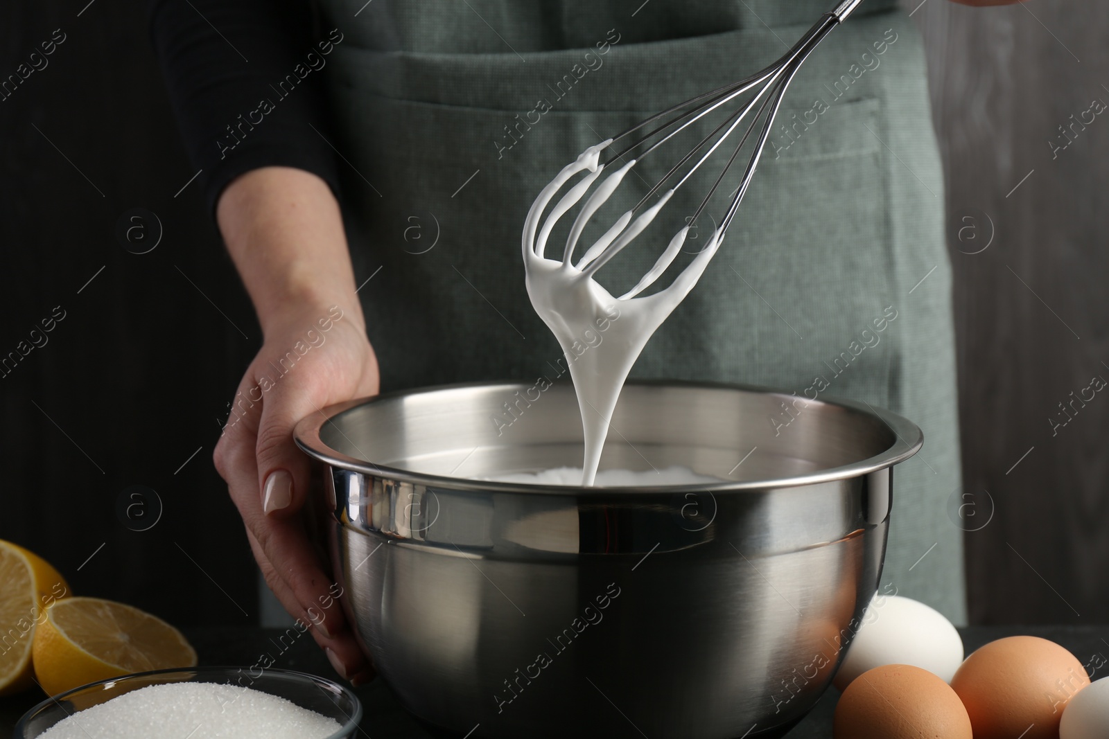 Photo of Woman making whipped cream with whisk at black table, closeup