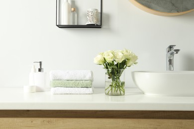 Photo of Bouquet of beautiful roses in vase and bath accessories near sink in bathroom