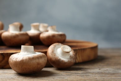 Photo of Fresh champignon mushrooms and cutting board on wooden table, space for text