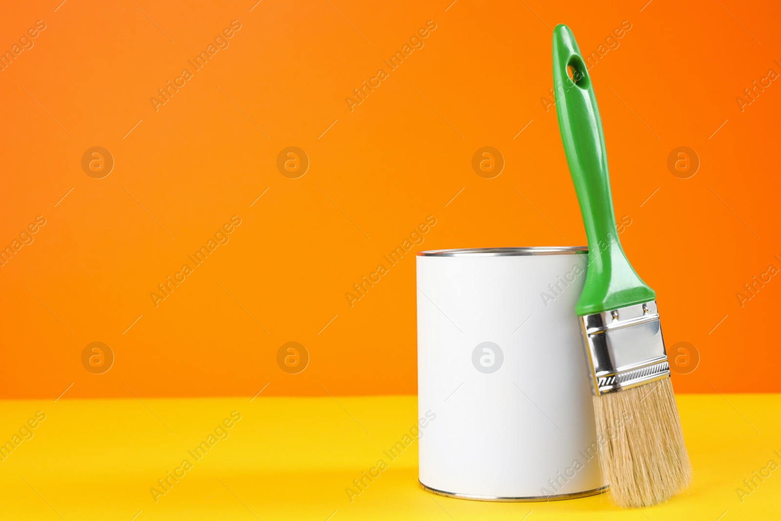 Photo of Blank can of paint with brush on table against color background. Space for text