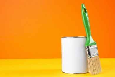 Blank can of paint with brush on table against color background. Space for text