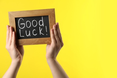 Woman holding blackboard with words GOOD LUCK on yellow background, closeup. Space for text