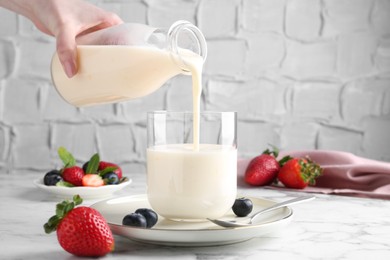 Photo of Woman pouring tasty yogurt into glass at white marble table, closeup