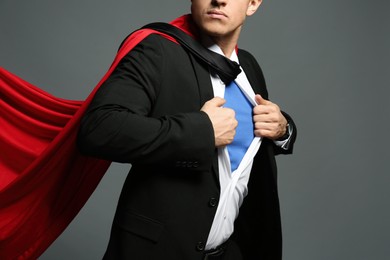 Photo of Businessman in superhero cape taking suit off on grey background, closeup