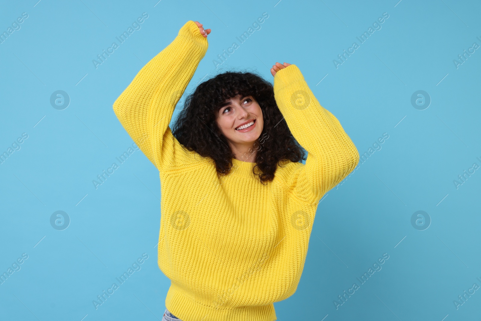 Photo of Happy young woman in stylish yellow sweater on light blue background