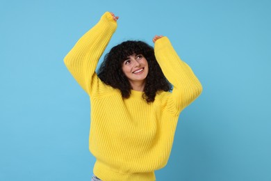 Happy young woman in stylish yellow sweater on light blue background