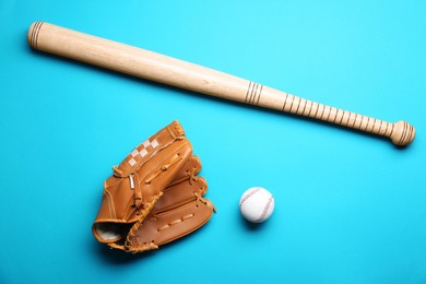 Baseball glove, bat and ball on light blue background, flat lay