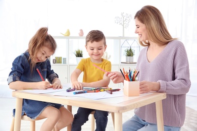 Cute little children and their nanny drawing at home