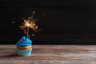 Delicious birthday cupcake with sparkler on table