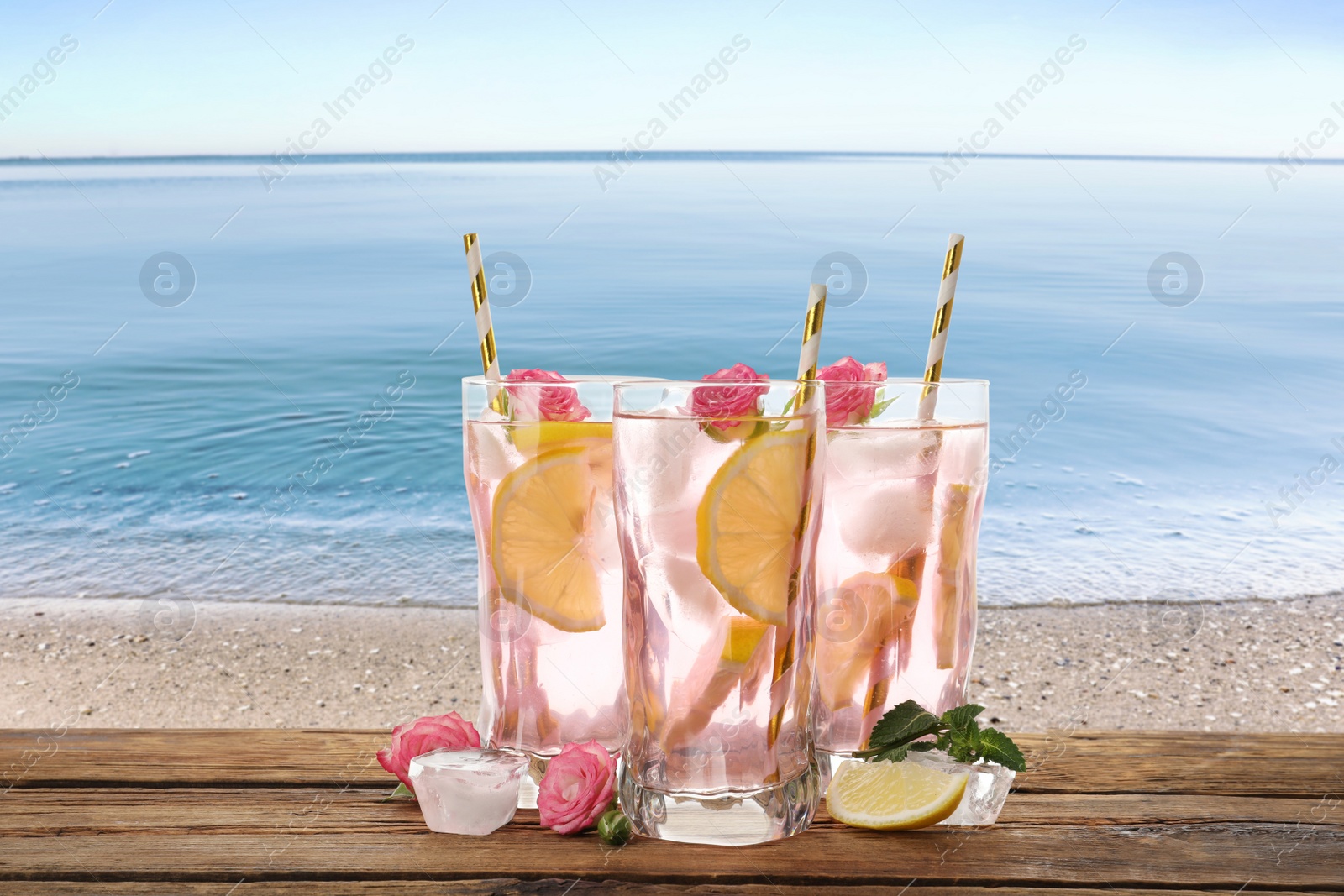 Image of Tasty refreshing drink on wooden table against sandy beach