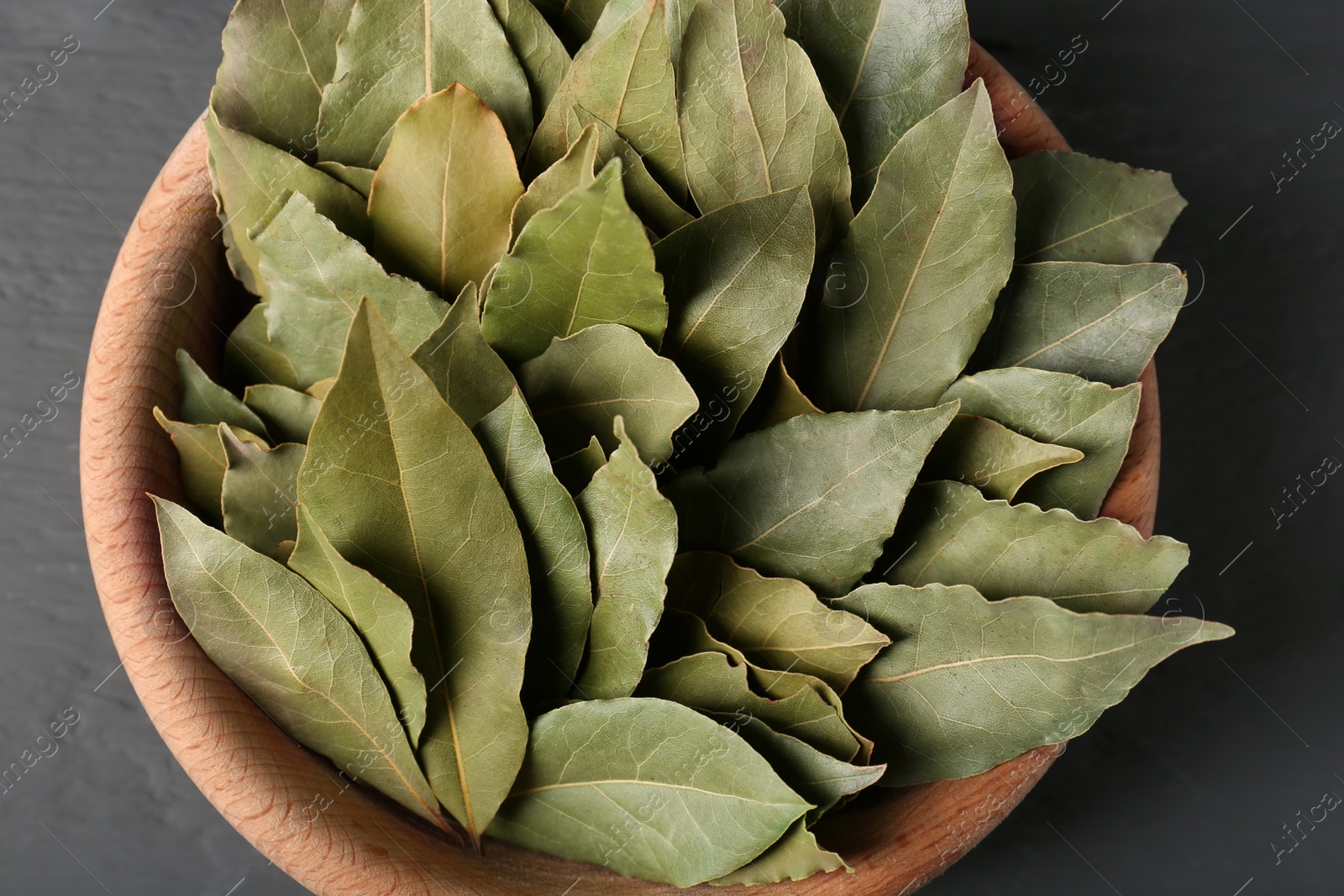 Photo of Aromatic bay leaves in wooden bowl, top view