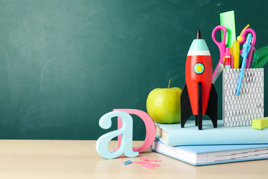 Photo of Bright toy rocket and school supplies on wooden desk. Space for text