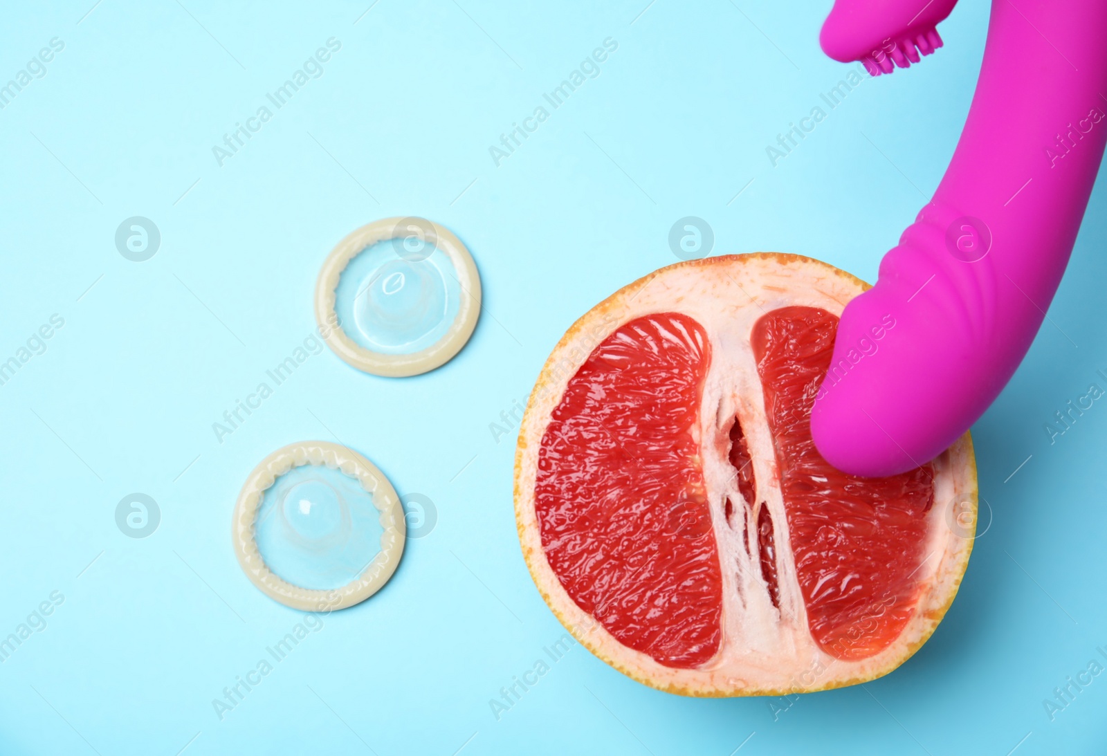 Photo of Half of grapefruit, purple vibrator and condoms on blue background, flat lay. Sex concept